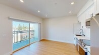 Located at 2301 Ulric St in San Diego, CA, this efficiently designed single-floor unit offers a clean, modern aesthetic throughout. Warm hardwood-style flooring runs continuously across the open layout, contributing to a cohesive and inviting atmosphere.

The kitchen is a standout feature, outfitted with crisp white shaker cabinetry extending to the ceiling, sleek quartz-style countertops, a glossy white subway tile backsplash, and a full suite of stainless steel appliances — including a French door refrigerator, electric range, over-the-range microwave, and dishwasher. A black matte hardware finish adds a contemporary contrast throughout.

The living area benefits from recessed lighting and a sliding glass door that opens to a private balcony with metal railing, allowing natural light to fill the space and offering open views of the surrounding San Diego neighborhood.

The bathroom is finished to a high standard, featuring a large walk-in shower enclosed by a sleek black-framed sliding glass door, a white toilet, and a vanity with a marble-style countertop. The consistent use of white tones and warm flooring throughout ties the space together with a fresh, modern sensibility.