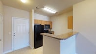 This 2-bedroom, 2-bathroom residence is a single-floor unit that offers a well-organized layout designed for comfortable everyday living. The kitchen is a central feature of the space, equipped with black appliances including a refrigerator, range, and over-the-range microwave. Light oak cabinetry provides generous storage, while the laminate countertops offer ample workspace. A peninsula with a granite-style surface extends from the kitchen, creating a natural divider between the kitchen and the adjoining living area while also serving as a convenient breakfast bar or serving space. The flooring in the kitchen features easy-to-maintain tile, contributing to a clean and practical aesthetic. The neutral wall tones throughout the unit create a bright and open atmosphere. The layout incorporates two full bathrooms, adding convenience for residents and guests alike. A standout feature of this unit is the inclusion of a private balcony, offering an outdoor extension of the living space — ideal for relaxing or enjoying fresh air. The single-floor design ensures seamless flow between all areas, making the space feel cohesive and accessible throughout.