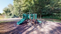 Situated at 95 S Westmoor Ave in Newark, Ohio, this single-story property provides a functional and community-oriented environment. The standout feature visible from the exterior is a well-equipped outdoor playground area, complete with a multi-component play structure finished in green. The structure includes dual slides, a tunnel, climbing elements, and connecting platforms, all set atop a rubber mulch surface that provides safe, cushioned ground cover for active use. The playground is framed by a generous canopy of tall, mature trees that offer natural shade and a lush, green backdrop, creating an inviting and protected outdoor atmosphere. The tree coverage lends the space a sense of seclusion and natural calm, making it particularly suitable for recreational activities. The interior areas of the property, while not fully illuminated in available imagery, reflect a compact, single-floor layout with defined room partitions as suggested by the floor plan. Overall, the property combines practical indoor space with a notably appealing and thoughtfully equipped outdoor recreational area, well-suited for community or family-oriented use in the Newark, Ohio area.