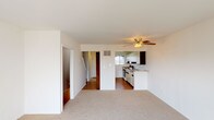 This three-floor space offers a straightforward, functional layout spread across multiple levels. The main living area features neutral-toned carpet, white walls, and a ceiling fan with light fixture, creating a bright and open atmosphere. The space flows into a kitchen equipped with an electric coil range, granite-style laminate countertops, white upper cabinetry with wood accents, an overhead range hood, and hardwood flooring. A window above the counter brings in natural light. One living area features a full-width sliding glass door with vertical blinds, offering outdoor views and generous natural light.

The bedrooms are carpeted and well-sized, with clean white walls and ceiling fans. A notably spacious bedroom includes dual bi-fold closets providing substantial built-in storage. Additional rooms throughout feature standard closets with dark wood doors and wall-to-wall carpet.

The bathroom features a tub-shower combination with classic pale yellow ceramic tile surround. The basement level is unfinished, housing the water heater and exposed ductwork and framing, with a painted concrete floor and a small ground-level window, offering practical utility and potential storage space.