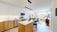Located at 347 N Queen St in the heart of Lancaster, PA, this thoughtfully designed one-bedroom, one-bathroom residence offers a contemporary living experience with efficient use of space throughout. The open-concept kitchen and living area serves as the focal point of the unit, featuring a striking two-tone kitchen with white upper cabinetry and warm wood-grain lower cabinets and island. A white quartz countertop, textured tile backsplash, and a full suite of stainless steel appliances — including a refrigerator, range, microwave, and dishwasher — complete the kitchen. A sleek linear pendant light anchors the island, which doubles as a dining and prep space. The living area is bathed in natural light from large floor-to-ceiling windows that frame views of the surrounding Lancaster cityscape, with light hardwood flooring extending throughout. The bedroom offers a cozy yet functional retreat, featuring a generous window with urban views and direct access to a dedicated closet. The bathroom is finished with large-format floor tiles, a wood-vanity with white countertop, a wide mirror, and a tiled walk-in shower, maintaining the modern aesthetic found throughout the home.