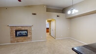 This single-story home offers a thoughtfully designed layout with a warm, neutral color palette throughout. The spacious living area immediately draws attention with its soaring vaulted ceiling, creating an open and airy atmosphere. A ceiling fan and elegant chandelier provide both function and style, while a striking stone-surround fireplace serves as a central focal point, adding character and warmth to the room. Soft, wall-to-wall carpeting extends across the living and bedroom areas, contributing to a comfortable feel. An arched passageway connects the living area to the rest of the home, adding an architectural touch of distinction. The kitchen is well-equipped with stainless steel appliances, including a gas range, built-in microwave, and refrigerator. Warm medium-toned wood cabinetry pairs with dark granite countertops, while stone tile flooring ties the space together. A large window over the sink brings in natural light. The bedroom offers a generous layout with carpeted floors and a sizable window fitted with vertical blinds. The bathroom includes a vanity with dark granite countertops, a tub-shower combination, and matching stone tile flooring, completing this cohesive and functional home.