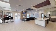 Located on Tutt Boulevard in Colorado Springs, Colorado, this single-story community clubhouse offers a well-appointed, open-concept interior designed for both relaxation and functionality. The expansive main living area serves as the centerpiece of the space, anchored by a dramatic floor-to-ceiling stacked stone fireplace with a mounted flat-screen TV above and a modern linear firebox. A large sectional sofa and area rug create an inviting lounge environment, while oversized windows and sliding glass doors to an outdoor patio fill the space with natural light and provide views of the surrounding community. A bold accent ceiling with a deep burgundy finish and a large ceiling fan adds architectural contrast to the otherwise light, neutral palette throughout.

The fully equipped kitchen is a standout feature, showcasing grey shaker-style cabinetry, white quartz countertops, stainless steel appliances including a gas range and refrigerator, and a stainless steel wall-mount range hood. A generously sized kitchen island with bar seating and sleek pendant lighting above makes the space ideal for entertaining and communal gatherings. Light wood-tone luxury vinyl flooring flows seamlessly throughout the entire space, tying together the modern aesthetic. A private office or workspace is also accessible from the main area, offering a quieter setting for focused tasks.