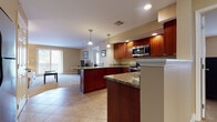 This single-floor residence offers a thoughtfully designed open-concept layout that seamlessly connects the kitchen, dining, and living areas. The kitchen is a standout feature, showcasing rich cherry wood cabinetry, granite countertops, stainless steel appliances including a range and microwave, and large-format tile flooring. A central island with pendant lighting extends the counter space and serves as a natural divider between the kitchen and the adjoining living area. The living room is warm and inviting, finished with plush carpeting and bathed in natural light from a set of sliding glass doors that open to a private balcony overlooking a serene, tree-lined backdrop. The two bedrooms are carpeted and comfortably sized, each offering closet storage and large windows that allow ample natural light. The primary bathroom features matching cherry vanity cabinetry with granite countertops and tile flooring, maintaining the consistent design language found throughout the home. A second full bathroom mirrors this aesthetic with a double-sink vanity, tile floors, and a clean, functional layout. Warm neutral tones on the walls throughout create a cohesive and calming atmosphere across the entire residence.