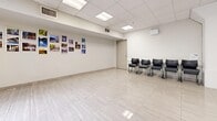 This single-floor commercial space in California offers a clean, functional layout well-suited for a variety of professional uses. The interior is defined by its open, expansive floor plan, finished with light-toned polished tile flooring that reflects the abundant overhead lighting throughout.

The space is divided into two primary areas. The main hall is generously proportioned, providing ample room for gatherings, workstations, or events. A suspended drop ceiling features recessed panel lighting alongside a prominent skylight, flooding the area with natural light and enhancing the airy, open ambiance. Neutral beige and white walls keep the environment bright and adaptable.

A secondary area serves as a reception or waiting zone, equipped with seating along the walls and a utility table, making it practical for client-facing operations. A doorway connects to a back room with built-in shelving, adding organizational utility to the space.

Additional features include HVAC venting integrated into the ceiling, a fire safety system, and clearly marked emergency exits. The workstation section is outfitted with multiple computer desks and ergonomic chairs, reflecting readiness for office or training use. Decorative photo displays add a welcoming touch to the otherwise minimal aesthetic. Overall, the space presents a well-maintained, versatile commercial environment with a clean and professional atmosphere.