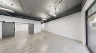 Located at 4015 133rd St SE in Mill Creek, Washington, this single-floor commercial space offers a versatile and modern industrial aesthetic throughout. The open main areas feature polished concrete floors and exposed ceilings with visible ductwork and structural beams painted dark gray, lending a clean, contemporary warehouse character. Linear LED lighting runs overhead, providing even, bright illumination throughout. Large floor-to-ceiling windows and a glass-paneled entry door front the space, allowing natural light to flood the interior and providing views to the exterior surroundings.

Sliding barn-style doors connect the main open areas, offering flexible room division. The fully equipped kitchen includes warm wood-toned cabinetry with matte black hardware, gray countertops, a white tile backsplash, a stainless steel sink, electric range, refrigerator, dishwasher, and a range hood. A dedicated laundry room houses a full-size Whirlpool front-loading washer and dryer. The bathroom features polished concrete floors, blue-painted walls, a wall-mounted sink with mirror, and an open shower area with grab bars. Two hallways connect the support spaces efficiently. The overall layout is well-suited for a variety of commercial or creative uses.
