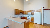 Located at 555 Seventh St NW in Grand Rapids, Michigan, this two-floor loft-style space blends industrial character with functional living. The layout spans two levels, showcasing a compelling mix of original architectural elements and updated interior finishes throughout.

The kitchens are well-appointed with warm oak cabinetry extending to impressive heights, light-toned countertops, and white appliances including an electric range, microwave, refrigerator, and dishwasher. A peninsula counter provides additional workspace and a casual dining option. Hardwood flooring runs through the kitchen and bathroom areas, adding warmth and continuity.

Living and sleeping areas are carpeted and feature exposed brick accent walls that highlight the building's industrial heritage. Large multi-pane windows allow natural light to fill the space while offering views of the surrounding greenery. Exposed wooden beam ceilings and visible ductwork reinforce the loft aesthetic, particularly on the upper level.

The bathrooms are clean and functional, each featuring a full tub-shower combination, oak vanity with a single sink, a large mirror, and hardwood floors. Closet space is available in the bedroom areas, with track lighting and exposed conduit adding to the industrial design character. This space offers a distinctive urban loft experience in the heart of Grand Rapids.