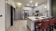 This single-floor residence in Sandy Springs, GA, offers a thoughtfully designed open-concept layout that seamlessly connects the kitchen, dining, and living areas. The kitchen is a standout feature, outfitted with gray shaker-style cabinetry, crisp white quartz countertops, and a full suite of stainless steel appliances, including a French door refrigerator, electric range, built-in microwave, and dishwasher. A central island with bar seating and pendant lighting above adds both functionality and style, while light wood-look flooring runs throughout the main living areas, enhancing the bright, airy atmosphere.

The living room is anchored by a dramatic tray ceiling with an elegant chandelier, deep green accent walls, and large windows with sliding glass door access to an outdoor space, allowing generous natural light and views of surrounding greenery. The bedroom continues the tray ceiling detail and features plush carpet, multiple windows, and a spacious walk-in closet with built-in wire shelving. The adjoining bathroom offers gray vanity cabinetry, a large mirror, and light wood-look flooring, with a decorative curtained shower area. The overall ambiance is contemporary yet warm, blending modern finishes with comfortable, livable design.