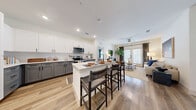 This thoughtfully designed 2-bedroom, 2-bathroom residence offers a cohesive and modern living experience across a single floor. The open-concept layout seamlessly connects the kitchen, dining, and living areas, all unified by warm-toned hardwood-style flooring. The kitchen is a standout feature, showcasing two-tone cabinetry with white upper cabinets and gray lower cabinets, stainless steel appliances, a clean white countertop, and a central island with bar seating — ideal for both meal prep and casual dining. The living room is bright and welcoming, with large French doors that invite natural light and provide outdoor access, complemented by a ceiling fan overhead. Both bedrooms are carpeted and comfortably sized, with large windows that bring in natural light. The primary bedroom includes its own closet with built-in shelving for organized storage. The bathrooms feature gray shaker-style vanities with black hardware, wood-look flooring, and a tub-shower combination. An additional closet with open shelving provides further storage throughout the residence. The overall ambiance is clean, contemporary, and move-in ready, with a neutral color palette that offers a versatile backdrop for any style.