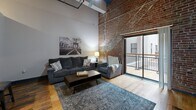 Located in the heart of downtown St. Louis on Washington Avenue, this one-bedroom, one-bathroom loft unit blends industrial heritage with modern finishes. The open-plan living, dining, and kitchen area serves as the centerpiece of the home, anchored by dramatic soaring ceilings with exposed wood beams and visible ductwork that pay homage to the building's historic origins. Rich hardwood floors run throughout, complementing the striking exposed brick wall that spans the living area. Sliding glass doors open to a private balcony overlooking a bright interior atrium, flooding the space with natural light.

The kitchen is well-appointed with white cabinetry, dark granite countertops, black matte hardware, a double stainless steel sink, and a full suite of stainless appliances. A peninsula counter provides additional workspace and casual dining.

The bedroom features elevated ceilings, hardwood flooring, a mirrored sliding-door closet, and a calm, private atmosphere. The bathroom is clean and functional, offering a large sliding-glass enclosed shower, a wood-toned vanity, and stone-look tile flooring. Additional conveniences include in-unit laundry, a hallway, and two closets, making this a complete and practical urban retreat.