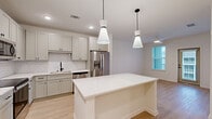 Located at 100 Wilton Cir S in Palm Coast, Florida, this single-floor, one-bedroom, one-bathroom residence offers a well-designed layout that maximizes functionality. The open-concept living area seamlessly connects the kitchen, dining, and living spaces, creating a bright and cohesive environment. The kitchen is a standout feature, boasting soft gray shaker-style cabinetry, white quartz countertops, a classic subway tile backsplash, a black matte sink faucet, and a full suite of stainless steel appliances including a French door refrigerator, range, microwave, and dishwasher. A large central island with pendant lighting above adds both prep space and a casual dining option. Light wood-style flooring runs throughout the main living areas, complementing the clean, neutral color palette. The bedroom offers a generous footprint, carpeted flooring, a ceiling fan, and a window with natural light. Three closets, including a walk-in with wire shelving, provide ample storage. The bathroom features subway-tiled tub and shower surround with matte black fixtures and light wood flooring. A dedicated laundry area and an exterior door from the living space add everyday convenience to this thoughtfully appointed home.