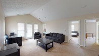 Located at 1905 N Lincoln Ave in Urbana, IL, this single-floor unit showcases a thoughtfully designed open-concept layout that maximizes the sense of space throughout. The living and kitchen areas flow seamlessly together beneath striking vaulted ceilings, which are accentuated by track lighting that illuminates the entire common area. Large French doors in the living room invite natural light and provide access to an outdoor patio, further enhancing the open, airy atmosphere.

The kitchen is equipped with white cabinetry, white appliances including a range, microwave, and refrigerator, and features a generously sized peninsula with a double sink and bar seating — ideal for casual dining or entertaining. Hardwood-style flooring grounds the kitchen, transitioning to plush carpeting throughout the living and bedroom areas.

The bedrooms are well-proportioned, each offering natural light through blinded windows and closet storage. The unit includes two bathrooms: a full bath with a tub-shower combination and tile flooring, and a half bath with a vanity and tile floors. Neutral warm tones and vaulted ceilings carry throughout the unit, creating a cohesive and comfortable living environment.