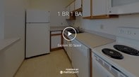 Located at 1600 Hennepin Ave in Minneapolis, Minnesota, this single-floor unit offers a well-organized layout with distinct living, kitchen, and bathroom areas. The living space is generously sized, featuring neutral wall-to-wall carpeting that creates a warm, understated ambiance. A standout architectural detail is the ornate dark wood fireplace mantel, accented by distinctive teal tilework, lending a classic, historic character to the room. A window alongside the fireplace allows natural light to filter in, with views of surrounding greenery.

The kitchen is efficiently designed with a galley-style layout, offering ample wood-trimmed cabinetry in both upper and lower configurations, light-toned countertops, and white appliances including a refrigerator, electric range, dishwasher, and over-range microwave. Tile flooring runs throughout the kitchen, providing a practical, easy-to-maintain surface. A pass-through counter connects the kitchen to the main living area, enhancing the open feel of the space.

The bathroom is clean and straightforward, featuring tile flooring, a single-sink vanity with wood cabinetry, a large mirror, and a full tub-shower combination. The overall unit presents a functional and livable space with a notable historic accent.