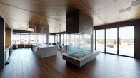 Located at 351 S Jackson St in Denver's vibrant Washington Park neighborhood, this contemporary single-floor amenity space offers a seamlessly integrated open-plan design that blends indoor comfort with outdoor living. The interior is anchored by a striking, glass-enclosed double-sided fireplace with a dark brick chimney column, serving as a dramatic architectural centerpiece that divides the lounge and gathering areas while maintaining visual connectivity throughout.

The gourmet kitchen is a standout feature, equipped with a large concrete-topped island, professional-grade gas cooktop, double wall ovens, stainless steel range hood, and open shelving set against textured blue-gray brick accent walls. Rich, wide-plank hardwood flooring runs throughout the space, complemented by warm wood-paneled ceilings that add depth and a refined natural aesthetic.

Multiple lounge seating areas are thoughtfully arranged to take advantage of floor-to-ceiling glass walls, which frame expansive city views of the Denver skyline and surrounding neighborhood. Sliding glass doors provide direct access to a generous outdoor terrace, outfitted with additional seating, landscaped planters, and string lighting—ideal for gatherings at any time of day. Exposed concrete columns punctuate the interior, reinforcing the space's modern industrial character while adding structural interest.
