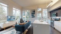 This single-floor residence showcases a contemporary design characterized by an abundance of natural light and treetop views visible from nearly every room. The open-concept layout seamlessly connects the kitchen, dining, and living areas, creating a cohesive and functional space. Dark hardwood flooring anchors the main living area, complementing the neutral tones of the walls and ceilings.

The kitchen is a standout feature, equipped with stainless steel appliances, a combination of white lower cabinetry and rich dark wood upper cabinets, and a generously sized island with a crisp white countertop and integrated sink. Pendant lighting above the island adds a refined finishing touch.

The living area is framed by a broad bank of windows that flood the space with natural light while providing views of the surrounding evergreen trees. Elevated ceilings enhance the sense of openness throughout.

The bedrooms are well-proportioned, each featuring large windows with treetop or neighborhood views. One bedroom is finished in soft sage green tones, lending a playful character. A full bathroom includes a soaking tub and shower combination with clean white finishes. Overall, the space delivers a bright, modern aesthetic with thoughtful details throughout.