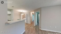 This single-floor residence offers a practical and cohesive layout across two bedrooms and one full bathroom. The open-concept living, dining, and kitchen area forms the heart of the unit, finished with durable hardwood-style flooring throughout. The kitchen is equipped with white cabinetry, light stone-look countertops, stainless steel appliances including a refrigerator and dishwasher, and a sink with ample workspace. A peninsula counter separates the kitchen from the dining area, which features a decorative pendant light fixture. An in-unit washer and dryer are tucked behind bifold doors in this same zone, adding everyday convenience.

The living room opens to an outdoor area via a sliding glass door framed by vertical blinds, allowing natural light and views of surrounding greenery. A ceiling fan overhead adds functionality to this space.

Both bedrooms are carpeted and finished in neutral tones, each offering windows for natural light. The primary bedroom includes a walk-in closet with wire shelving on multiple walls. The full bathroom features a single-sink vanity with stone-look countertop, a large mirror, wood-style flooring, and a tub-shower combination. Textured ceilings are consistent throughout the unit.