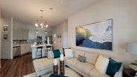 This well-appointed single-floor residence offers a thoughtfully designed open-concept layout that seamlessly connects the living, dining, and kitchen areas. The living room is bright and welcoming, featuring large windows dressed with stylish curtains that invite abundant natural light, complemented by warm wood-tone flooring and contemporary décor including a striking large-scale wall art piece.

The kitchen is outfitted with light gray flat-front cabinetry, quartz countertops, a subtle tile backsplash, and a full suite of stainless steel appliances including a refrigerator, microwave, dishwasher, and range. A kitchen island with bar seating adds both functionality and a social focal point.

Two generously sized bedrooms each offer plush carpeting, large windows with ample natural light, and a calm, neutral color palette. Both bathrooms are finished with granite-topped vanities, gray wood-look tile flooring, modern cabinetry, and a tub-shower combination with tile surround. One bathroom features a double-sink vanity, providing added convenience.

A dedicated in-unit laundry space houses a full-size side-by-side washer and dryer with overhead shelving. Throughout the residence, the consistent use of neutral tones, modern fixtures, and quality finishes creates a cohesive and refined living environment.