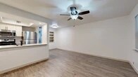 This 1-bedroom, 1-bathroom unit offers a clean, modern aesthetic with consistent wood-look plank flooring carried throughout every room. The combined kitchen and living area forms the heart of the unit, where an open pass-through counter connects the kitchen to the living space, creating an airy, connected feel. The kitchen is equipped with stainless steel appliances, including a full-size refrigerator, and features recessed lighting and white cabinetry. The living room is bright and open, accented by a ceiling fan with integrated lighting and a set of built-in shelving niches that add both character and functional storage. The spacious bedroom comfortably accommodates a full furniture arrangement and includes its own ceiling fan, a window with blinds for natural light and privacy, and direct access to a closet and the hallway. The bathroom is a standout feature, showcasing a tiled shower surround with a wood-grain pattern in neutral tones, complemented by a built-in niche for storage and oil-rubbed bronze fixtures that add a refined touch. A hallway connects all rooms efficiently, and a dedicated closet provides additional storage. The unit's cohesive neutral color palette and modern finishes create a clean, move-in-ready living environment.
