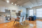Located at 735 Broad St in the heart of downtown Chattanooga, this single-floor loft-style unit blends industrial character with modern comfort. Warm hardwood floors run throughout, complementing the cool gray walls and exposed ceiling ductwork that give the space its distinctive urban aesthetic.

The open-plan kitchen and dining area form a central hub, featuring white cabinetry, stainless steel appliances including a range and dishwasher, a double sink, and ample counter space. A solid wood dining table with white chairs sits adjacent, ideal for gathering. Track lighting overhead highlights the generous ceiling height in this area.

The living room is bright and welcoming, benefiting from large windows that allow natural light to pour in. A mounted flat-screen television anchors the space, complemented by hardwood floors and a comfortable seating arrangement.

Multiple bedrooms provide private retreats, each furnished with well-appointed beds and soft lighting. The bedrooms feature tall ceilings, natural light from windows, and a calm, neutral palette. Two bathrooms with shower-tub combinations and hardwood flooring serve the unit, maintaining the clean, consistent design language found throughout the entire space.