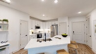 Located at 401 Oberlin Road in Raleigh, NC, this single-floor, 2-bedroom, 2-bathroom residence offers a thoughtfully designed layout with modern finishes throughout. The open-concept kitchen is a standout, featuring white shaker cabinetry, a herringbone tile backsplash, stainless steel appliances, and a large quartz waterfall island with an undermount sink and seating — ideal for both cooking and entertaining. Light hardwood-style flooring flows through the main living areas, adding warmth to the clean, contemporary aesthetic. The living room is bright and inviting, with a ceiling fan, sliding glass doors that open to a private balcony, and serene outdoor views of mature trees. The primary bedroom offers generous proportions, plush carpeting, and access to a well-appointed en-suite bathroom featuring a dual-sink vanity with white cabinetry, quartz countertops, and wood-look flooring. The second bedroom is equally comfortable, also finished with carpet and natural light. A spacious walk-in closet with wire shelving provides ample storage. The dedicated laundry room houses a full-size side-by-side washer and dryer. Clean white walls and recessed lighting throughout create a bright, cohesive ambiance across the entire residence.