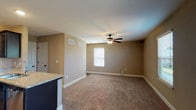 This three-story home offers a thoughtfully designed layout across multiple levels, combining practical finishes with comfortable living spaces. The kitchen is a standout feature, showcasing dark espresso cabinetry, granite countertops, a full suite of stainless steel appliances including a refrigerator, electric range, built-in microwave, and dishwasher, all complemented by warm hardwood-style flooring and recessed lighting. The living areas are generously proportioned, with neutral-toned carpet, ceiling fans with light fixtures, and natural light provided by windows with blinds. One living space includes sliding door access, suggesting outdoor connectivity. The bedrooms continue the carpeted aesthetic, each equipped with ceiling fans and closet access. The home includes multiple bathrooms: a primary bath featuring a dual-sink vanity with white countertops, dark cabinetry, hardwood-style flooring, and a glass-enclosed shower, while additional bathrooms offer single-sink vanities and tub/shower combinations. Warm beige and tan wall tones carry throughout the home, lending a cohesive and inviting ambiance. The lower level provides a spacious bonus room with ample square footage, a ceiling fan, and an electrical panel, offering flexible use as a recreation room or additional living space.