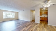 This single-floor residence features a thoughtfully designed open-concept layout that connects the main living area to the kitchen, creating a cohesive and functional flow throughout the space. The expansive living room is finished with wood-tone luxury vinyl plank flooring that extends throughout the common areas, complemented by neutral beige walls and a textured ceiling. A large window allows natural light to fill the room, enhancing its open and airy feel.

The kitchen is positioned adjacent to the living area and features warm oak-toned cabinetry, white countertops, a stainless steel sink, and stainless steel appliances including a dishwasher and range. Ample upper and lower cabinetry provides generous storage.

The bedrooms are carpeted for comfort and include windows fitted with horizontal blinds. One bedroom benefits from a spacious walk-in closet outfitted with wire shelving and hanging rods, offering practical storage solutions. Additional closet space is present in other areas of the unit as well.

The bathroom includes a wood-tone vanity with a white countertop, a glass-enclosed shower, and wood-look flooring that ties into the overall aesthetic of the space. Throughout, the unit maintains a clean, neutral palette suited to a variety of interior styles.