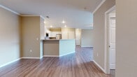 This single-floor residence is designed with an open-concept layout that seamlessly connects the kitchen and living areas, creating a spacious and functional flow throughout. The living area features wood-style laminate flooring in a warm neutral tone, crown molding, recessed lighting, and a ceiling fan, contributing to a clean and comfortable ambiance.

The kitchen is well-appointed with white shaker-style cabinetry, granite-style countertops, and stainless steel appliances including a range, over-the-range microwave, and refrigerator. A peninsula with a raised countertop serves as a natural divider between the kitchen and living space, offering additional workspace and seating potential.

The bedrooms are carpeted in a neutral beige tone, each featuring windows with blinds that allow natural light while maintaining privacy. Closet space is provided within the bedrooms for convenient storage.

The bathroom includes a granite-style vanity top with white cabinetry, a large mirror, a toilet, and a full soaking tub with shower. Wood-style flooring extends into the bathroom, maintaining a cohesive aesthetic. Throughout the unit, neutral warm-toned walls provide a versatile backdrop suitable for a variety of interior styles.
