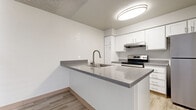 This single-floor unit offers a clean, modern aesthetic throughout, with thoughtful finishes and a functional layout evident from the 3D floor plan. The kitchen serves as a central highlight, featuring a peninsula with stone-speckled quartz countertops, an undermount stainless steel sink with a pull-down faucet, crisp white cabinetry with contemporary hardware, and a full suite of stainless steel appliances including an electric range and refrigerator. Light wood-look flooring runs through the kitchen and living areas, contributing to a bright and cohesive feel. The living room benefits from a large sliding glass door that fills the space with natural light and provides direct views to the outdoors. The entry area transitions seamlessly into the main living space, also finished with the same wood-look flooring. The bedrooms are carpeted for comfort, offering neutral tones and ample natural light through blinds-fitted windows. One bedroom features a wide sliding-door closet, providing generous storage. The bathroom is outfitted with a full-size soaking tub and shower combination, finished with clean white tile surround, wood-look flooring, and brushed nickel fixtures, completing this well-maintained and move-in ready space.