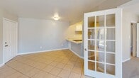Located at 630 Brent St in Winston-Salem, NC, this single-floor unit offers a practical and well-organized layout designed for comfortable everyday living. The kitchen is outfitted with crisp white cabinetry extending to the upper walls, light-toned countertops, a stainless steel double sink, a black dishwasher, and a range, all set over easy-to-clean tile flooring. A peninsula counter connects the kitchen to an adjacent dining or living area, which is accessible through a charming French door with glass pane detailing. The open living and dining areas feature neutral-toned tile flooring and large windows dressed with vertical blinds, allowing natural light to filter throughout. The bedrooms are finished with plush wall-to-wall carpeting and feature windows with exterior views, providing a quiet and comfortable retreat. One bedroom includes a spacious sliding-door closet, offering ample storage. The full bathroom is appointed with a rich wood-framed vanity mirror, a single-sink vanity with brushed nickel fixtures, and a full tub-shower combination. A dedicated utility area houses the water heater and electrical panel, with built-in shelving for added storage. The consistent neutral color palette and clean finishes throughout give the space a move-in-ready appeal.