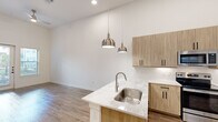 This thoughtfully designed single-floor residence offers a cohesive blend of modern aesthetics and functional living across its well-appointed rooms. The open-concept kitchen serves as a central highlight, featuring light wood cabinetry with matte black hardware, a quartz waterfall island with a stainless steel undermount sink, subway tile backsplash, and stainless steel appliances including a refrigerator, electric range, and built-in microwave. Dual brushed nickel pendant lights hang above the island, adding warmth and style. Wood-look flooring flows throughout the main living areas, creating a seamless and cohesive look. The entry area impresses with soaring ceilings and built-in open shelving in a slate blue finish, adding both storage and character. The bedroom is carpeted for comfort and benefits from natural light through multiple windows with blinds. The bathroom is distinctively finished with slate blue cabinetry, marble-look countertops, black hardware, and a striking geometric patterned tile floor, along with a soaking tub. A dedicated laundry area with hookups and a closet with a hanging rod offer practical storage solutions. Throughout, the bright white walls and clean lines lend the space a fresh, contemporary ambiance.