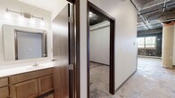 Located at 801 Second Ave N in Moorhead, MN, this one-bedroom, one-bathroom unit offers a distinctive loft-style aesthetic rooted in industrial character. The open living and kitchen area immediately draws the eye with its exposed concrete ceiling, visible ductwork and piping, and a striking original brick accent wall that speaks to the building's historic bones. Large, multi-pane windows flood the main living space with natural light, creating an airy atmosphere despite the unit's intimate footprint. The kitchen is equipped with stainless steel appliances — including a range, microwave, and refrigerator — alongside warm wood-toned cabinetry and a dishwasher, balancing functionality with style. A structural column anchors the open-plan space, adding to the loft's urban charm. The bedroom is a well-proportioned, quiet retreat with neutral walls and exposed ceiling details consistent with the rest of the unit. The bathroom features a walk-in shower stall, toilet, and vanity in a clean, understated design. A dedicated laundry area includes a stacked Whirlpool washer and dryer unit with adjacent wire shelving for added storage convenience. Throughout, the raw concrete-style flooring and industrial finishes give this unit a bold, creative character well-suited to those who appreciate urban, adaptive-reuse living.