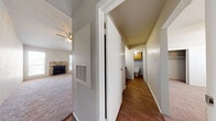 This single-story residence is organized around a central hallway with dark hardwood-style flooring that connects the entry, bathroom, and living areas. The entry foyer is framed by a paneled white front door and textured walls, establishing a clean, utilitarian aesthetic throughout.

The living room is a standout space, featuring a vaulted ceiling with a ceiling fan, plush carpet, and a stone-surround fireplace that serves as the room's focal point. Large windows and a sliding glass door with vertical blinds allow natural light to fill the space and provide views of the outdoors. A pass-through opening with a wood-toned cabinet above connects the living area to the adjacent kitchen space, allowing for easy communication between rooms.

Each bedroom is carpeted and equipped with a ceiling fan, a window with blinds for natural light, and a sliding closet with built-in shelving for storage. The rooms offer a comfortable and functional layout.

The bathroom features wood-tone cabinetry at the vanity and above the tub, a tub-shower combination, and hardwood-style flooring, maintaining a cohesive, practical design. Textured walls are consistent throughout the unit, adding subtle visual depth to the overall interior.