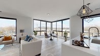 Unit 209 at Fifty58 is a thoughtfully designed single-floor residence that combines contemporary architecture with an open, airy aesthetic. The living and dining area is a standout feature, anchored by expansive floor-to-ceiling corner windows framed in matte black that flood the space with natural light and provide sweeping outdoor views of the surrounding landscape. Light-toned hardwood flooring runs throughout, complementing the neutral palette of the interior.

The kitchen is outfitted with two-tone cabinetry—high-gloss white upper cabinets paired with wood-grain lower cabinetry—and a generous island with a quartz countertop and seating for multiple guests. Stainless steel appliances, including a French door refrigerator and gas range, complete the functional yet stylish space. Geometric pendant lighting adds an industrial accent above the island.

The primary bedroom features sliding glass doors opening to a private balcony, offering additional outdoor access and natural light. It is served by a sleek en-suite bathroom with an all-white tile walk-in shower and glass enclosure. A second bedroom provides a comfortable, well-proportioned retreat. A second bathroom features large-format tile, a soaking tub, and chrome fixtures, maintaining the unit's clean, modern character throughout.