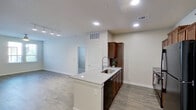 This single-story residence is designed with a clean, contemporary aesthetic and a practical open-concept layout. The kitchen serves as a central hub, anchored by a peninsula-style island with a light granite countertop and an undermount sink with a pull-down faucet. Rich, warm-toned wood cabinetry provides generous storage, complemented by black appliances including a refrigerator, range, and built-in microwave. Recessed lighting illuminates the space efficiently throughout.

The kitchen flows seamlessly into the living area, which features wood-style plank flooring and neutral wall tones, creating a bright and cohesive atmosphere. A ceiling fan with integrated lighting is present in the main living space, which also benefits from multiple windows that invite natural light and outdoor views.

The bedrooms are finished with plush carpeting, ceiling fans, and windows fitted with blinds, offering a comfortable and quiet retreat. Two full bathrooms mirror each other in style, each featuring a tub-shower combination with tile surround, wood-toned vanity cabinetry, a single sink, and wood-style flooring. One bathroom also includes access to a walk-in closet. The overall design emphasizes neutral tones, functional finishes, and a well-organized flow throughout.