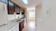 This single-floor unit offers a practical and comfortable layout designed to maximize everyday living. The galley-style kitchen is a standout feature, showcasing rich dark-espresso cabinetry with brushed nickel hardware, light granite-style countertops, a stainless steel sink, and a white gas range with oven. The kitchen flows seamlessly toward a bright living area, where a large window invites ample natural light and views of the surrounding greenery.

The bedrooms are well-sized and thoughtfully laid out, with some featuring durable hardwood-style flooring and others offering soft, neutral-toned carpeting for added comfort. Multiple windows fitted with blinds ensure each room benefits from natural light while maintaining privacy. The hallway corridor connects the living spaces in an efficient, easy-to-navigate arrangement.

The bathroom is clean and functional, featuring a white vanity with ample counter space, a wall-mounted mirror with integrated lighting, and a shower stall with tiled surround. Neutral, warm-toned walls are carried throughout the entire unit, creating a cohesive and inviting atmosphere. The combination of hardwood-style floors in key living areas and plush carpet in others adds both practicality and warmth to this move-in-ready space.