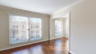 Located in the Manor Jr community in Los Angeles, CA, this single-floor unit offers a well-appointed layout highlighted by rich, dark hardwood flooring that flows seamlessly throughout the living areas. Crown molding adds a refined architectural touch to each room, complementing the neutral, warm-toned walls that create a clean and inviting atmosphere.

The living area is generously proportioned, featuring large windows fitted with horizontal blinds that allow abundant natural light to filter in while offering views of the surrounding neighborhood. An elegant arched doorway serves as a distinctive architectural detail, connecting the living space to adjoining rooms and adding a classic design element to the interior.

The galley-style kitchen is efficiently designed, featuring granite-look countertops, white cabinetry extending to ceiling height, a double-basin stainless steel sink, and white appliances including a range, refrigerator, and built-in microwave. The hardwood flooring continues into this space, maintaining visual consistency throughout.

A dedicated vanity area with a tiled countertop, built-in drawers, and a large wall mirror with overhead lighting provides a functional and well-lit grooming space. Throughout the unit, clean white trim and baseboards frame each room, contributing to a cohesive and polished overall presentation.
