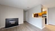 This single-floor, 2-bedroom, 1-bathroom residence offers a well-organized layout designed to maximize functionality. The living room serves as the central gathering space, featuring light gray laminate flooring, neutral-toned walls, and a striking black-framed fireplace as a focal point. Vertical blinds frame a sliding glass door that draws in natural light and provides outdoor access. A textured ceiling adds subtle architectural character to the space.

The kitchen is accessible via a pass-through counter opening from the living area, creating an open, connected feel. It features warm honey-toned cabinetry, light countertops, a tile backsplash, black appliances including a refrigerator and range, and laminate flooring that carries through from the main living space.

Both bedrooms are carpeted and finished with the same neutral wall tones found throughout the unit. Each room receives natural light through windows fitted with horizontal blinds. The primary bedroom includes a dedicated closet. A hallway connects the bedrooms to the shared full bathroom, which is outfitted with a tub-shower combination featuring gray tile surround, wood-toned cabinetry, and light countertops. The overall ambiance is clean, bright, and move-in ready.