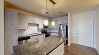 Located at 704 15th St in Durham, NC, this single-floor residence offers a well-designed layout with modern finishes throughout. The open-concept kitchen serves as the focal point of the living area, showcasing light wood cabinetry that extends to the ceiling, dark granite countertops, and a full suite of stainless steel appliances including a refrigerator, electric range, microwave, and dishwasher. A central island with a matching granite surface provides additional prep space and a natural gathering point, illuminated by stylish pendant lighting overhead. Track lighting further enhances the kitchen's functionality. Rich hardwood-style flooring flows throughout the main living and kitchen areas, adding warmth and continuity to the space. The living area is bright and airy, with large windows fitted with blinds that allow for ample natural light, complemented by a ceiling fan for year-round comfort. The bedroom features plush carpet flooring, a ceiling fan, and a generous window with an outdoor view. A spacious walk-in closet outfitted with multi-tiered wire shelving and hanging rods offers exceptional storage. The bathroom is finished with large-format stone tile surrounding a full soaking tub and shower combination, creating a clean and classic aesthetic throughout.