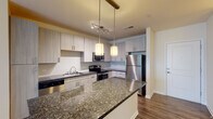 Located at 704 15th St in Durham, NC, this single-floor residence offers a well-designed layout with modern finishes throughout. The open-concept kitchen serves as the focal point of the living area, showcasing light wood cabinetry that extends to the ceiling, dark granite countertops, and a full suite of stainless steel appliances including a refrigerator, electric range, microwave, and dishwasher. A central island with a matching granite surface provides additional prep space and a natural gathering point, illuminated by stylish pendant lighting overhead. Track lighting further enhances the kitchen's functionality. Rich hardwood-style flooring flows throughout the main living and kitchen areas, adding warmth and continuity to the space. The living area is bright and airy, with large windows fitted with blinds that allow for ample natural light, complemented by a ceiling fan for year-round comfort. The bedroom features plush carpet flooring, a ceiling fan, and a generous window with an outdoor view. A spacious walk-in closet outfitted with multi-tiered wire shelving and hanging rods offers exceptional storage. The bathroom is finished with large-format stone tile surrounding a full soaking tub and shower combination, creating a clean and classic aesthetic throughout.