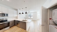 Located at 11701 Dionda Ln in Austin, TX, this efficiently designed single-floor unit offers a thoughtfully arranged open-concept layout that maximizes every square foot. The kitchen and living area flow seamlessly together, anchored by a striking peninsula with a white quartz countertop, an undermount stainless steel sink, and three pendant lights with matte black dome shades that serve as a visual centerpiece. The kitchen is outfitted with two-tone cabinetry — crisp white upper cabinets paired with warm taupe lower cabinets — set against a classic subway tile backsplash. Stainless steel appliances, including a range, over-the-range microwave, dishwasher, and refrigerator, complete the functional cooking space. Light hardwood-style flooring runs continuously throughout the main living areas, lending warmth and visual cohesion. The living area benefits from natural light through windows fitted with horizontal blinds, and a ceiling fan promotes comfortable airflow. The bathroom features matching taupe cabinetry with quartz countertops and tile flooring, maintaining the unit's consistent modern aesthetic. A dedicated closet provides practical storage. Clean white walls and a neutral palette throughout create a bright, airy ambiance well-suited to contemporary living in the Austin area.