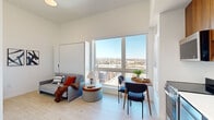 Located at 2095 19th St in Denver, CO, this efficiently designed studio offers a well-considered layout across a single floor, making smart use of every square foot. The living area is bright and airy, featuring light hardwood-style flooring, tall ceilings, and a large picture window that frames sweeping views of the Denver skyline and the Rocky Mountains beyond. A built-in Murphy bed integrates seamlessly into the living space, maximizing flexibility without sacrificing comfort. The room also accommodates a sofa, round ottoman, and a compact dining area with a wooden table and chairs — all bathed in abundant natural light. A wall-mounted TV and modern artwork complete the contemporary aesthetic. The kitchen is outfitted with warm wood upper cabinetry, dark lower cabinets, white countertops, and a full suite of stainless steel appliances including a range, microwave, dishwasher, and refrigerator. The bathroom features a floating wood vanity with a white countertop, dark-framed mirror, open shelving, and a clean white tiled tub-shower combination. The overall design is modern and minimal, with a neutral palette that enhances the sense of openness throughout.