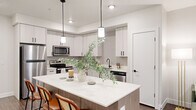 This well-designed 2-bedroom, 1-bathroom residence offers a thoughtful single-floor layout that maximizes functionality and style. The open-concept kitchen and living area serves as the heart of the home, featuring a large center island with quartz countertops and bar seating—ideal for both casual dining and entertaining. White shaker cabinetry with matte black hardware, a textured tile backsplash, and a full suite of stainless steel appliances, including a refrigerator, range, microwave, and dishwasher, complete the kitchen. Warm wood-look flooring flows throughout the main living areas, adding a contemporary yet inviting feel. The living room benefits from natural light through a large window with sheer curtains, creating a bright and comfortable atmosphere. The primary bedroom offers a well-proportioned layout with plush carpeting, a window for natural light, and direct access to a closet. The second bedroom is similarly finished with carpet and a window. The shared full bathroom features wood-toned cabinetry, a quartz-topped vanity with a single undermount sink, matte black fixtures, and a tub-shower combination. Clean white walls and recessed lighting throughout the space create a cohesive, modern aesthetic.