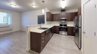 This single-floor unit offers a thoughtfully designed layout with a clean, modern aesthetic. The entry opens directly adjacent to the kitchen, which serves as a visual centerpiece of the space. The kitchen is outfitted with rich dark-wood cabinetry, light quartz countertops, stainless steel appliances including a range, microwave, and refrigerator, and a peninsula with an undermount sink — ideal for both cooking and casual dining. Light wood-look vinyl flooring extends through the kitchen and entry areas, lending a cohesive, contemporary feel.

The bedrooms are carpeted in neutral tones and receive natural light through windows fitted with horizontal blinds. At least one bedroom includes a closet with a built-in rod, providing practical storage. The neutral wall palette keeps the rooms feeling bright and versatile.

Two bathrooms serve the unit, each finished with wood-look vinyl flooring and neutral gray or white walls. Both include a tub-shower combination with a clean white surround. One bathroom features a dark-wood vanity with a white countertop, complementing the kitchen's design language. The overall ambiance of the unit is clean, contemporary, and move-in ready, with consistent finishes that create a unified, polished look throughout.
