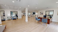 This thoughtfully designed single-floor facility spans a generous footprint and seamlessly blends wellness, comfort, and function. The layout flows through interconnected hallways linking distinct areas, each finished with a clean, contemporary aesthetic defined by white walls, recessed lighting, and drop-tile ceilings throughout.

The expansive fitness center is a standout feature, offering a comprehensive suite of exercise equipment including treadmills, ellipticals, cable machines, a smith machine with weight plates, dumbbells, resistance stations, and stability balls — catering to a full range of workout routines. Durable, neutral-toned carpet tiles cover the exercise floor, while framed artwork and blue accent walls add visual interest.

The open lounge and social areas feature light hardwood-style flooring, creating a bright and welcoming atmosphere. Comfortable seating arrangements with cream sofas, blue accent chairs, area rugs, and curated wall art give these spaces a polished, residential feel. A wall-mounted television anchors one of the gathering areas.

A private office space includes a executive desk setup with natural light from exterior-facing windows, complemented by a dedicated conference room with a round table and upholstered seating — ideal for meetings or consultations. Together, these spaces deliver a well-rounded, amenity-rich environment designed for both activity and community.