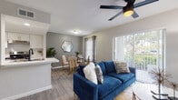 This single-floor residence offers a thoughtfully designed open-concept layout that seamlessly connects the living, dining, and kitchen areas. The living room is anchored by wood-look plank flooring, a ceiling fan, and a large sliding glass door that fills the space with natural light while providing outdoor views. The adjoining dining area flows naturally from the living room, creating a cohesive and functional common space.

The galley-style kitchen is finished with white shaker cabinetry accented by gold hardware, white countertops, a subway tile backsplash, and stainless steel appliances including a range, dishwasher, and refrigerator. A pass-through counter connects the kitchen to the main living area.

Two bedrooms are each carpeted and equipped with ceiling fans, sliding closet doors, and windows that allow natural light. The neutral tones and clean lines throughout both rooms contribute to a calm, restful atmosphere.

The full bathroom features a white vanity with gold-accented hardware, a large mirror, wood-look flooring, and a shower-tub combination. The overall design of the unit maintains a consistent contemporary aesthetic, with neutral gray walls and modern fixtures throughout.