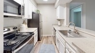 Located at 3006 E North St in Greenville, SC, this single-floor unit offers a clean, modern aesthetic throughout its well-designed layout. The open-concept living area features wood-style luxury vinyl flooring and neutral-toned walls, creating a bright and welcoming atmosphere. Large windows fitted with horizontal blinds allow generous natural light to fill the space while offering views of the surrounding greenery.

The kitchen is designed for functionality and style, featuring white shaker-style cabinetry with brushed nickel hardware, light quartz countertops, a stainless steel sink, and black appliances including a refrigerator, range, and over-the-range microwave. A peninsula counter connects the kitchen seamlessly to the living and dining areas, enhancing the open feel.

The bedrooms are finished with soft carpeting and include windows that bring in natural light, contributing to a comfortable and restful environment. The bathrooms are well-appointed with white vanity cabinetry, single-basin sinks, and full tub/shower combinations framed by white subway tile and complemented by wood-style flooring. A textured ceiling is present throughout the unit, adding a traditional residential character. The overall design balances practicality with contemporary finishes, making this a functional and visually cohesive living space.