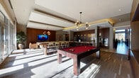 Located at 2–14 Station Drive in Westwood, Massachusetts, this single-story amenity facility presents a sophisticated, contemporary design throughout its expansive layout. The grand lobby sets a striking tone with soaring ceilings, a floor-to-ceiling stacked-stone fireplace flanked by rich wood paneling, large-format tile flooring, and sculptural pendant lighting. Plush seating arrangements and curated artwork create a welcoming, hotel-inspired atmosphere from the moment of entry.

The clubroom serves as a central social hub, featuring a billiards table, a wall-mounted television, and dining-height seating, all illuminated by modern globe chandeliers. Adjacent to it, a fully equipped gourmet kitchen showcases a generous marble-topped island with bar seating, warm walnut cabinetry, a mirrored tile backsplash, stainless steel appliances, and pendant lighting that adds a refined, polished finish.

A dedicated business lounge provides a productive environment with individual workstations, desktop computers, and comfortable lounge seating bathed in natural light from large windows overlooking lush outdoor greenery. A tiered screening room offers rows of plush cream-colored seating and a large display screen for private viewing experiences.

The fitness center is well-appointed with a broad range of cardio and strength equipment, floor-to-ceiling mirrors, and views to the outdoors. Throughout, warm wood accents, marble detailing, and carefully curated lighting unify the space with a cohesive, upscale ambiance.