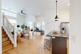 Located at 411 Charles Ave in Charlotte's vibrant Plaza Midwood neighborhood, this modern three-story home offers 2 bedrooms and 4 bathrooms across a thoughtfully designed layout. The ground floor provides a garage and entry, while the main living floor showcases a striking open-concept kitchen and living area. Soaring ceilings and large windows flood the space with natural light, highlighting wide-plank hardwood floors throughout. The kitchen is outfitted with crisp white cabinetry, quartz countertops, a bold dark-topped island with bar seating, stainless steel appliances, a black matte faucet, and a subway tile backsplash. Pendant lighting above the island adds a contemporary touch. The living area features oversized windows offering neighborhood views, with a ceiling fan completing the airy feel. Warm wood-tread stairs with clean white risers and a natural wood handrail connect all three floors. The upper level houses two well-appointed bedrooms, including a primary suite with dedicated closet space. The four bathrooms are elegantly finished, with one featuring geometric patterned tile flooring, a floor-to-ceiling tiled walk-in shower with glass door, and a dark stone vanity. A dedicated laundry room and utility space add practical convenience to this polished Charlotte home.