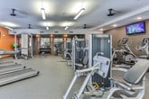 Located in Atlanta, GA, this fitness center offers a thorough and well-organized workout facility spread across a single floor. The space is designed to accommodate a wide variety of exercise routines, combining cardio and strength-training zones in a cohesive layout.

The cardio area features a row of treadmills positioned near windows that overlook an outdoor pool area, providing natural light and exterior views. A wall-mounted flat-screen television is conveniently placed nearby, adding an entertainment option during workouts. Ceiling fans provide additional air circulation throughout.

The strength-training section is generously equipped with Matrix-brand machines, a cable and pulley system, a dedicated free weights area with a full dumbbell rack, weight benches, and stability balls. Large wall mirrors enhance the sense of space and allow users to monitor their form.

The fitness center features a neutral color palette with warm orange accent walls, neutral carpet flooring, and a combination of recessed and pendant lighting that ensures even illumination throughout. A cubby storage area and a small service counter are also present, adding functional convenience. The overall ambiance is clean, modern, and practical, suited for comprehensive daily fitness routines.