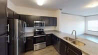This 1-bedroom, 1-bathroom unit offers a thoughtfully designed single-floor layout that balances comfort and functionality. The open-concept living and dining area features durable wood-look flooring, crown molding, and a ceiling fan, creating a bright and welcoming atmosphere. The space flows seamlessly into the kitchen, which is equipped with dark espresso cabinetry, granite-style countertops, stainless steel appliances including a refrigerator, range, and over-the-range microwave, and a double-basin sink — making it both practical and stylish.

The bedroom is a comfortable retreat, highlighted by plush carpeting, a ceiling fan, and a corner window arrangement that allows generous natural light and outdoor views. The bathroom is well-appointed with a dual-sink vanity set in dark cabinetry with granite countertops, a large mirror with vanity lighting, wood-look flooring, and direct access to a walk-in closet featuring built-in shelving and hanging rods. Additional storage is provided by louvered closet doors visible in the hallway area. The unit maintains a clean, neutral color palette throughout, with white walls and consistent trim work that lends a fresh, move-in ready feel to the entire space.